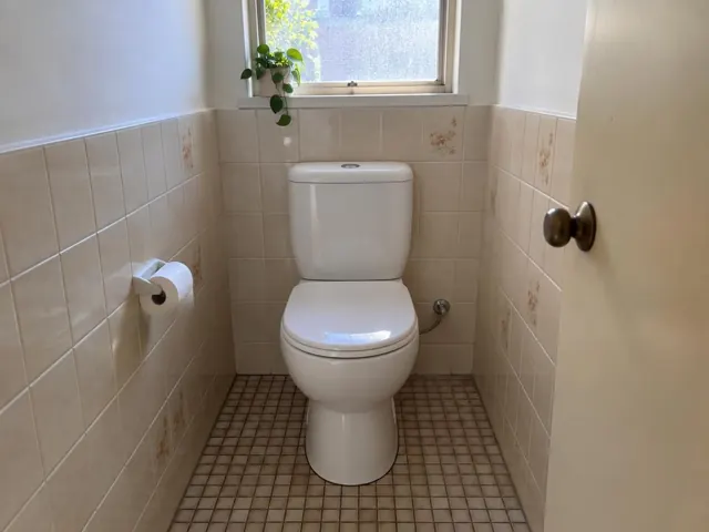 Clean white toilet in a tiled small bathroom with frosted window in Pagewood